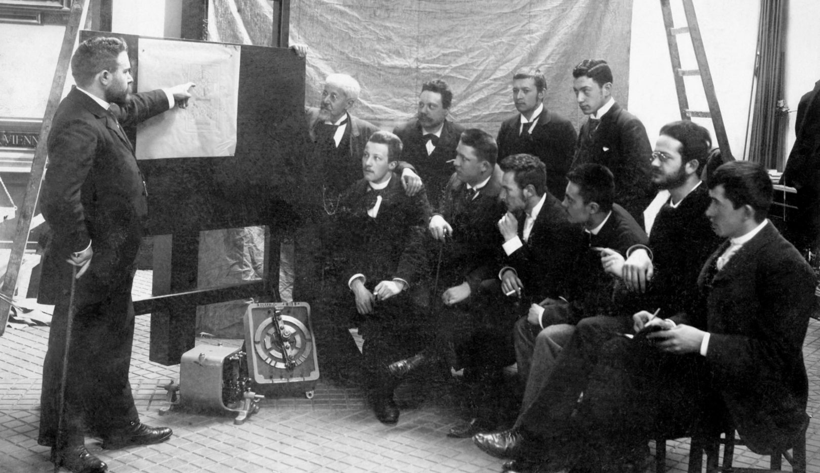 1895: Ferdinand Porsche (siedzący najbardziej po prawej) w firmie elektrycznej Bela Egger & Co, później Vereinigte Elektrizitäts AG, w wiedeńskiej dzielnicy Favoriten, podczas rozmów z szefem zakładu Wesselem i inżynierami.