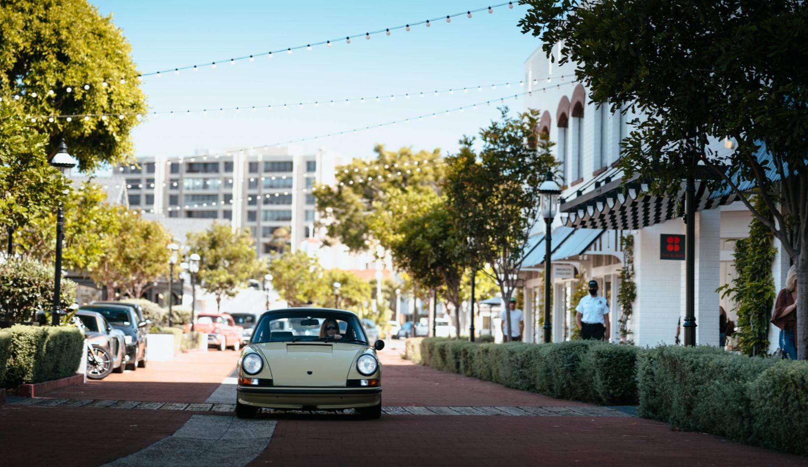 Promenade: Lara's classic car on the unhurried streets of Lido Marina Village in Newport Beach, framed by hedges and trees.