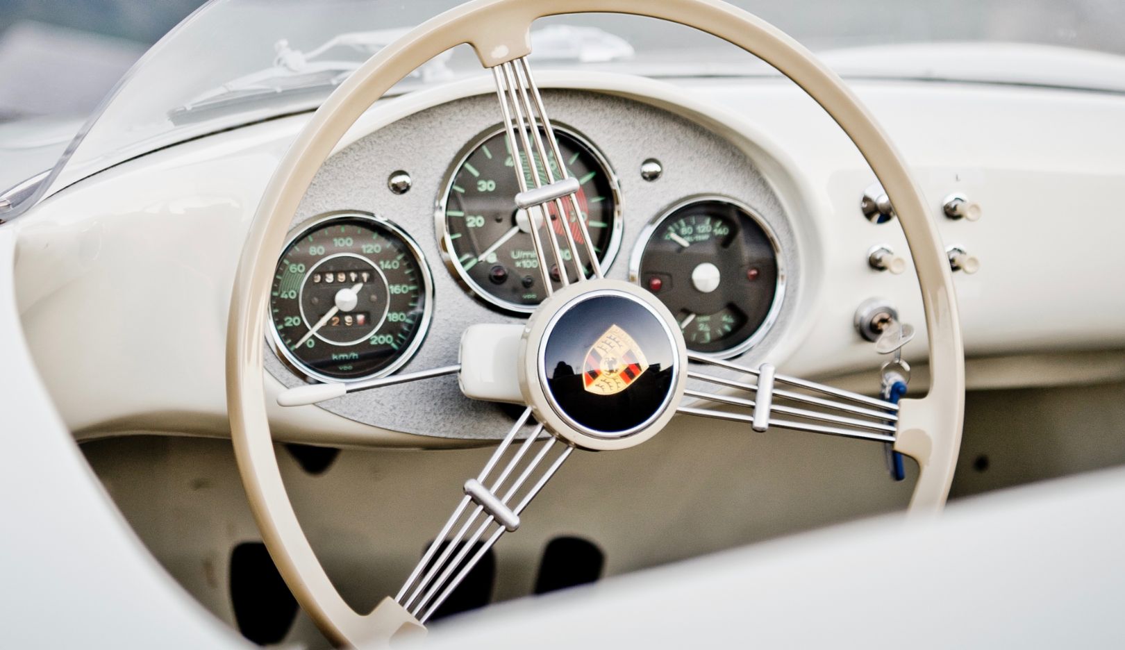 The narrow ivory-colored rim of the steering wheel and the triple spring spokes offer a clear view of the three instruments, with the rev counter at the center. Typical Porsche.