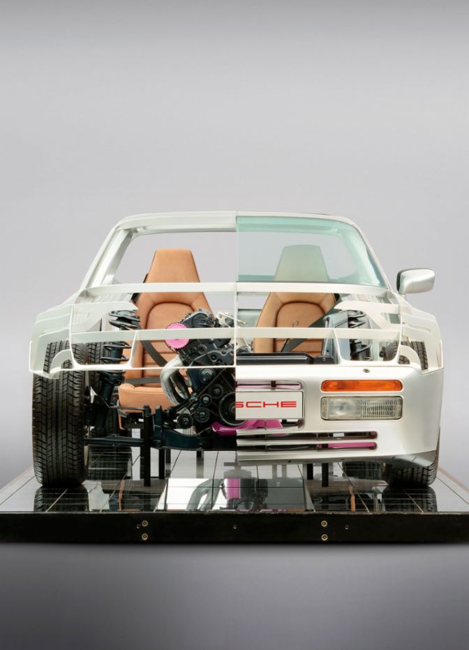 Eine Porsche 944-Technologieträger-Karosserie, die in der Mitte geschnitten und in zwei Hälften gezeigt wird, wobei die Technik im Inneren klar sichtbar ist. 