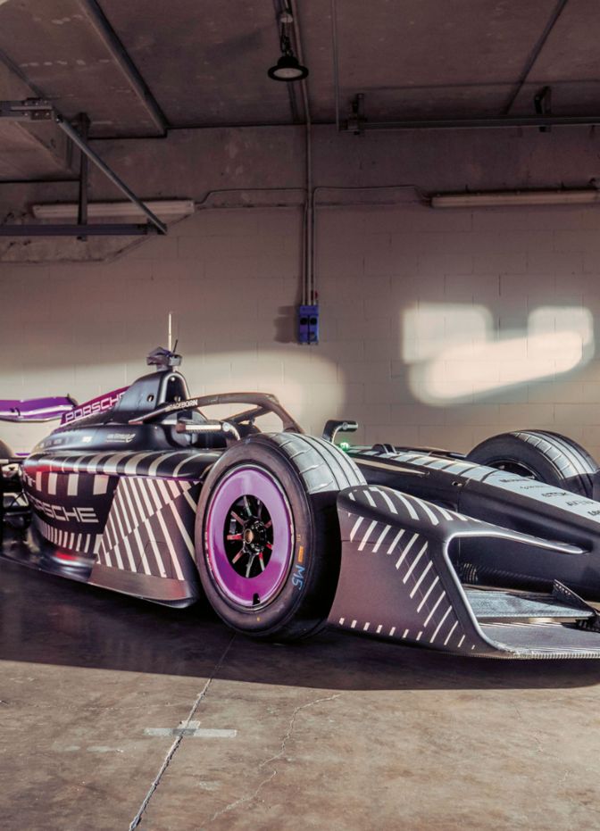 A formula race car is parked inside a garage with open doors and incoming light.