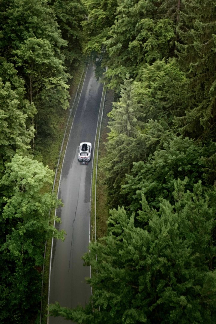 Ein weißes Auto mit Dachtbox fährt auf einer Straße, die durch einen Wald führt. 