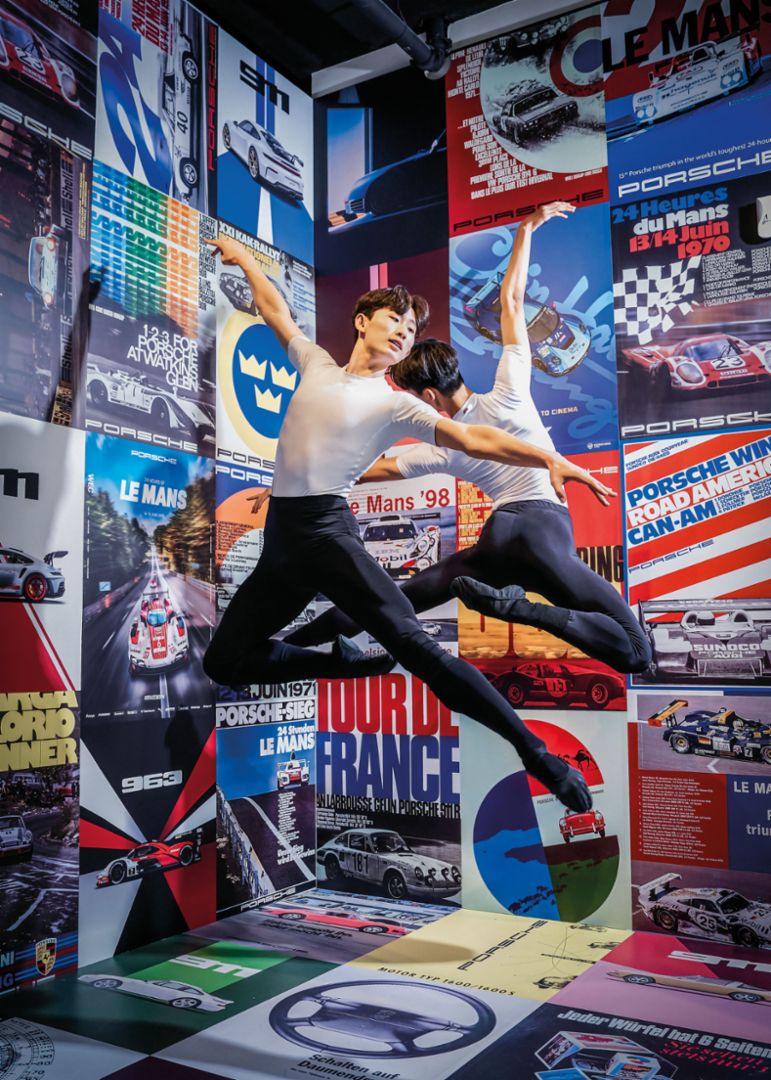 Ein Tänzer schwebt vor einer Wand aus farbigen Motorsport-Plakaten.