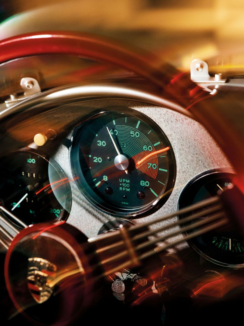 Ein klassischer Fahrzeugtacho zeigt beleuchtete Anzeigen und eine deutlich hervorgehobene Drehzahlmarkierung.