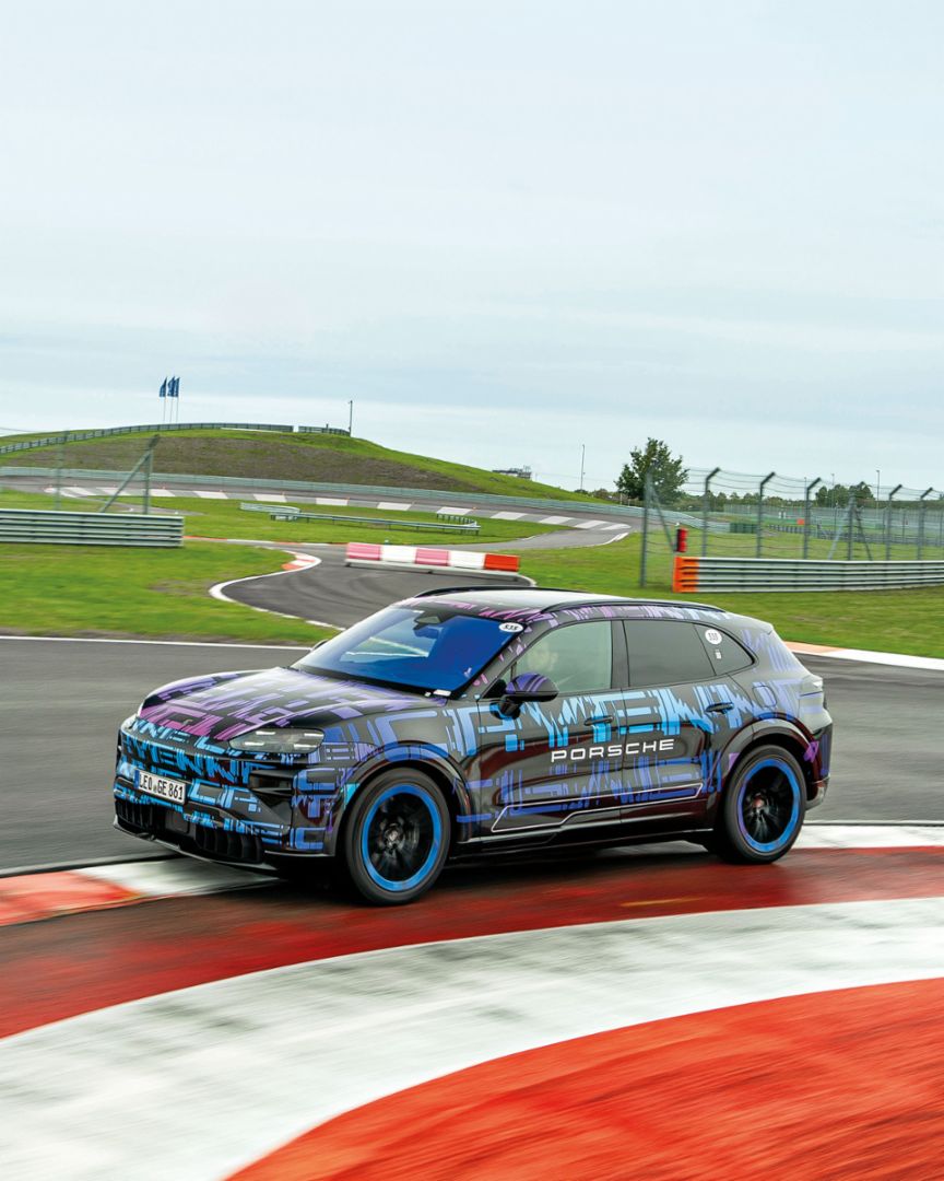 Ein getarntes Testfahrzeug fährt auf einer Rennstrecke durch eine Kurve.