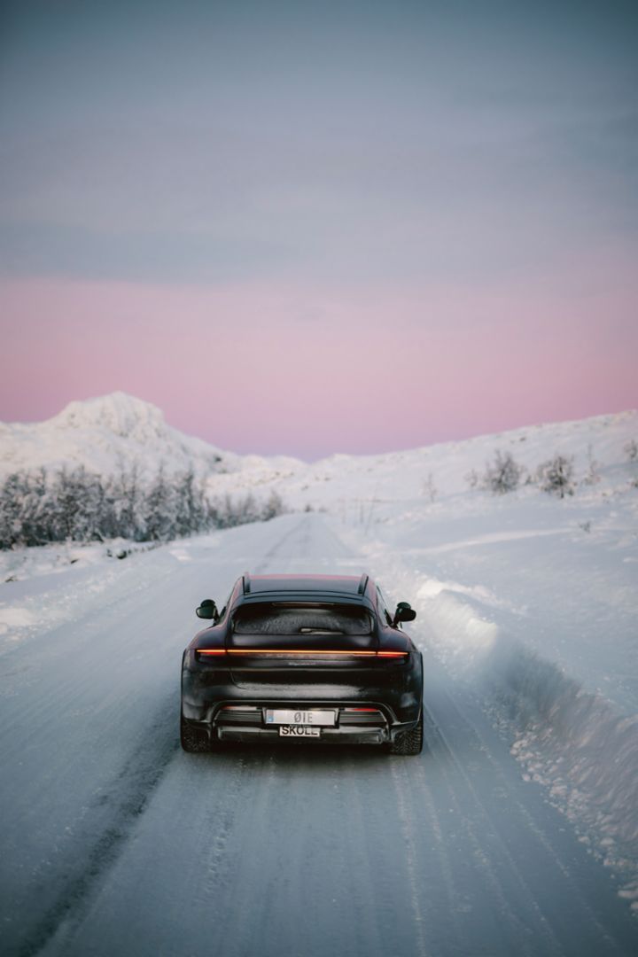 Ein Porsche Taycan fährt auf einer verschneiten Straße durch eine winterliche Landschaft, mit schneebedeckten Hügeln im Hintergrund.