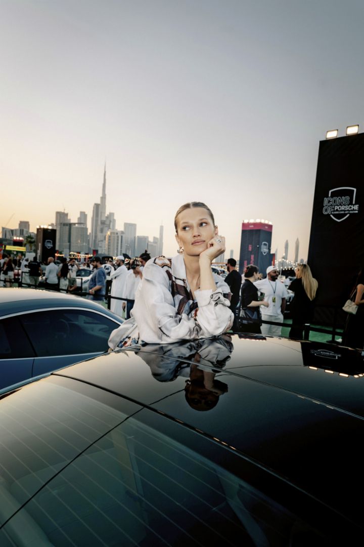 Ein Model posiert mit einem Porsche vor der Skyline von Dubai. 
