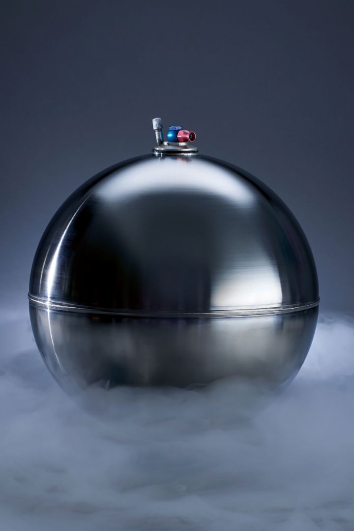 A spherical metal tank stands against a dark background surrounded by mist.