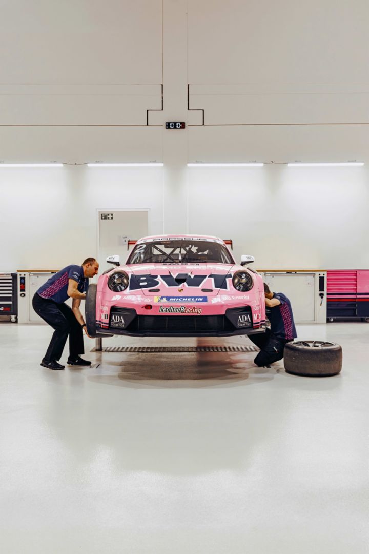 Two team members work on a pink race car elevated in a workshop.