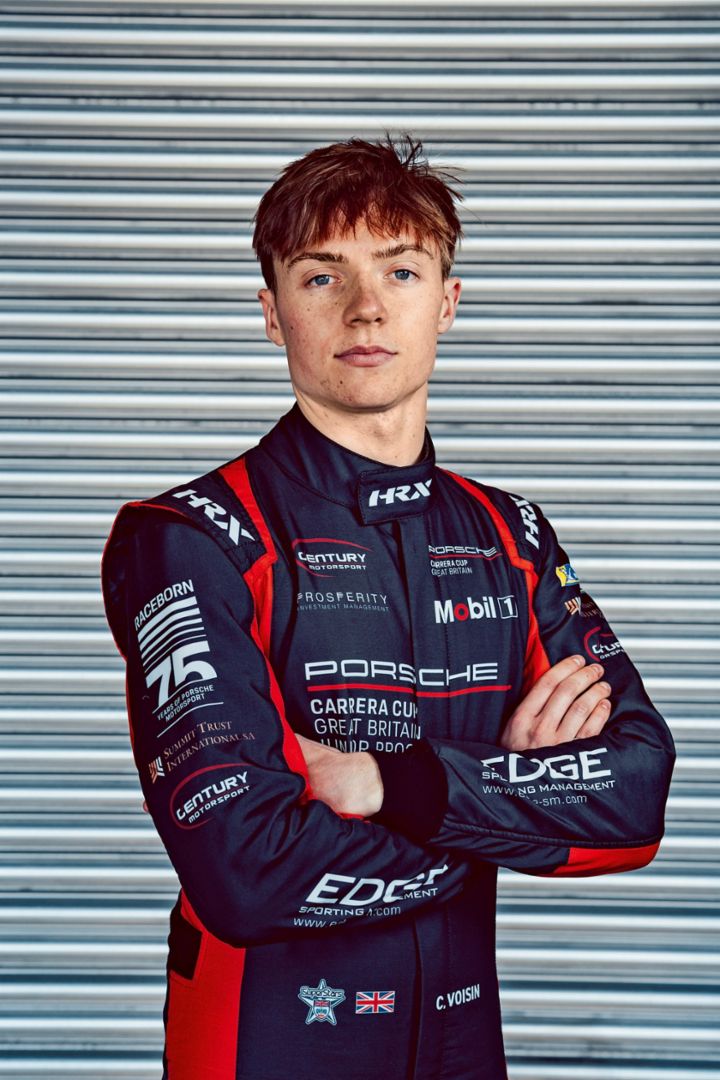 A person in racing gear stands with folded arms in front of a metal shutter.