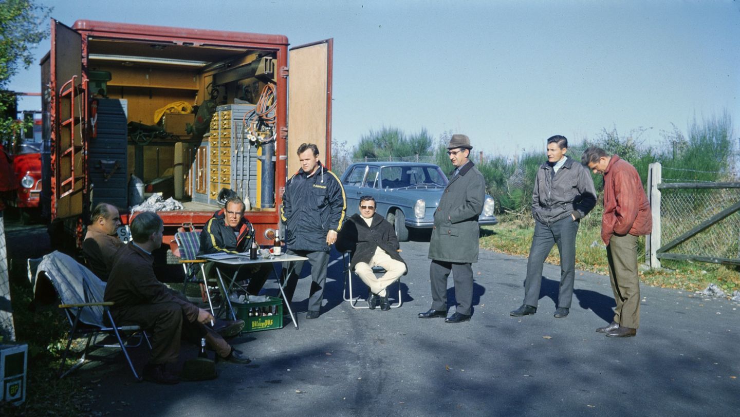 Marzo de 1968. Pruebas de manejo en el Circuito Sur de Nürburgring. En la mesa: Peter Falk. De izquierda a derecha Willi Enz, N.N., Peter Falk, Valentin Schäffer, Hans Herrmann, N.N. el ingeniero de pruebas Bilstein, Rolf Hannes y Jochen Freund.