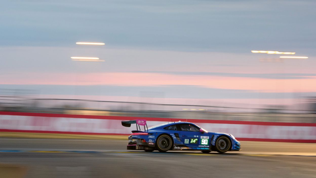 A dark blue race car with a distinctive rear wing and the starting number 90 speeds around a race track.
