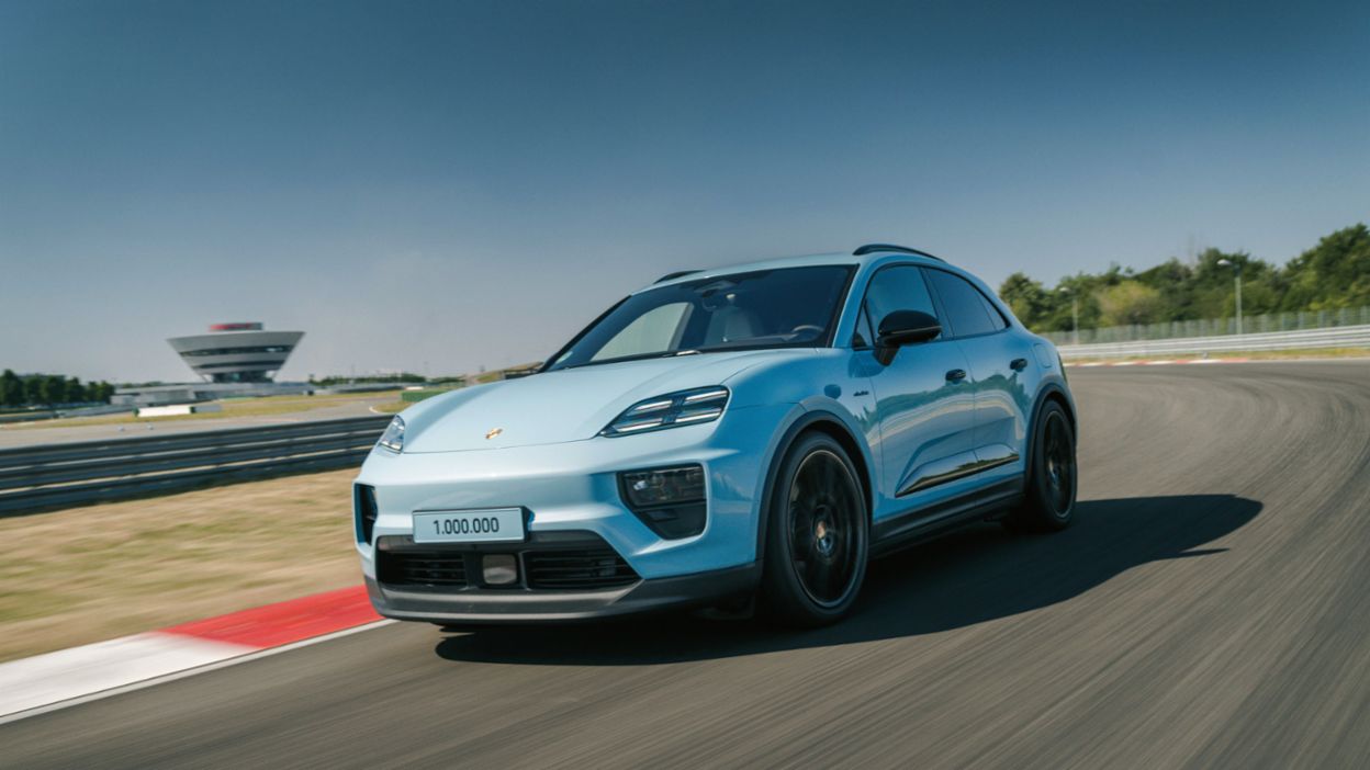 A Porsche Macan drives on a racetrack with a striking observation tower in the background and a “1,000,000” badge on the front of the vehicle.