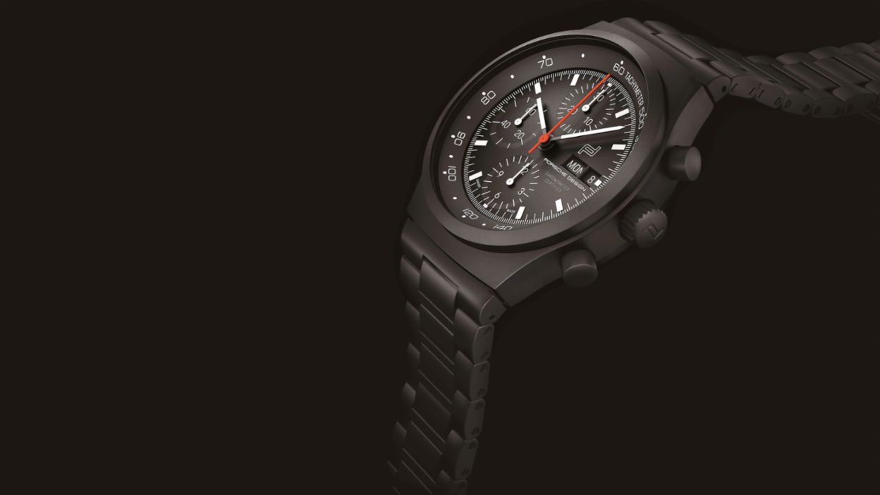 A wristwatch with a dark dial and strap is shown against a black background.