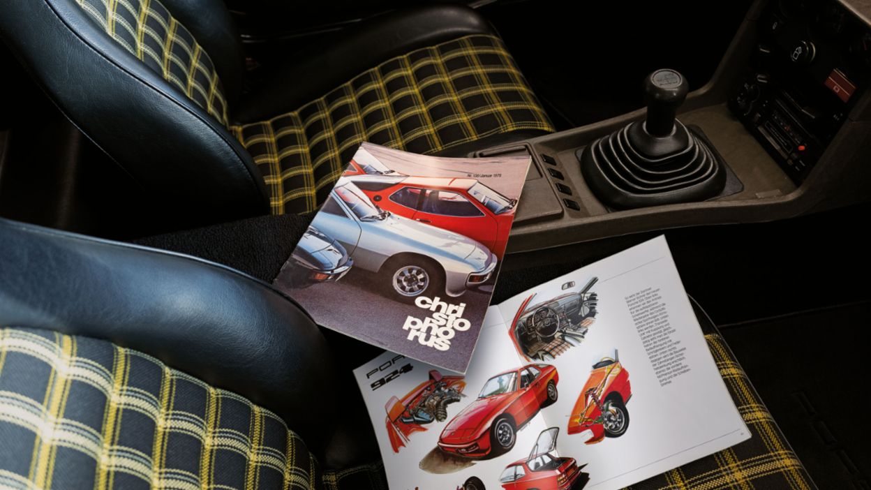 Innenaufnahme eines Porsche 924 mit einem Christophorus Magazin auf dem Beifahrersitz. Die Sitze sind mit gelb-schwarzem Karomuster bezogen und ein Schaltknauf ist sichtbar.
