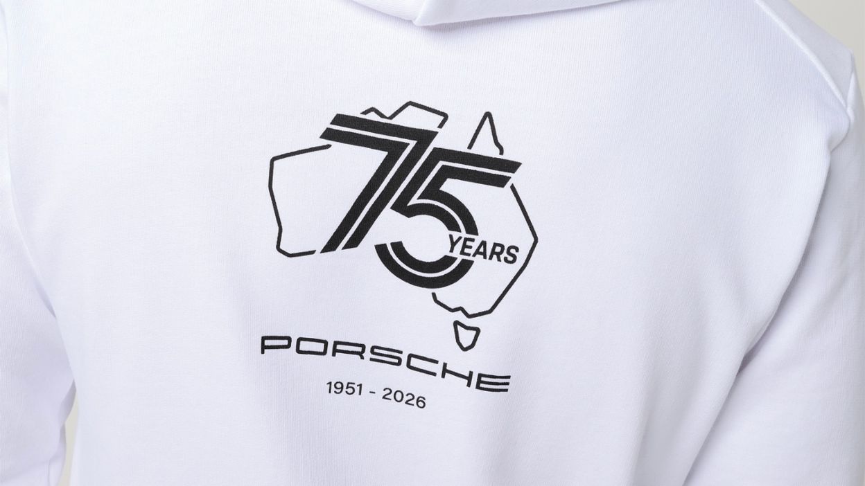 A person wears a white hoodie featuring a large anniversary graphic on the back.