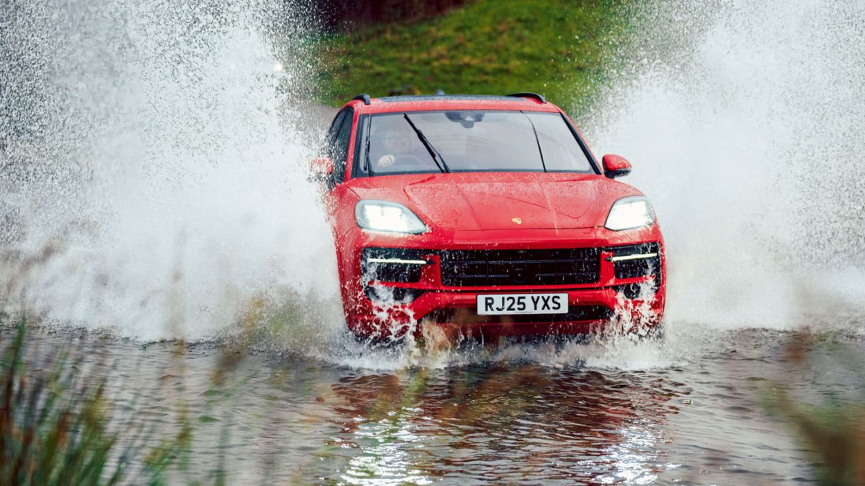 A red SUV drives through a water crossing, creating large splashes.
