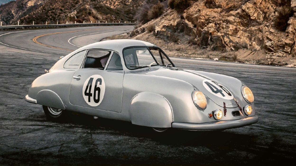Ein historischer Porsche steht auf einer kurvigen Bergstraße vor einer Felslandschaft bei Sonnenuntergang.