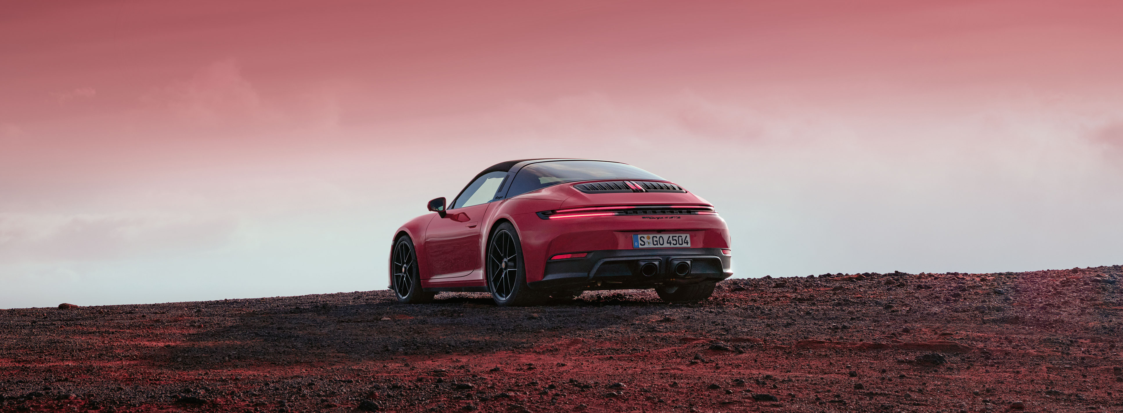 A Porsche 911 is parked on a desolate red landscape under a dramatic, crimson sky.